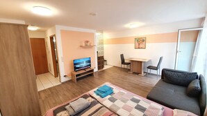 Ein modernes Wohnzimmer mit einer Couch, einem Fernseher, einem Esstisch mit Stühlen und einer kleinen Küchenzeile.