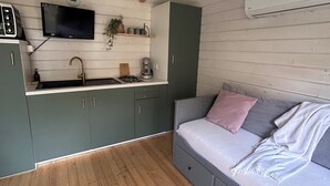 A compact room with a kitchenette, a bed, and a wooden floor.