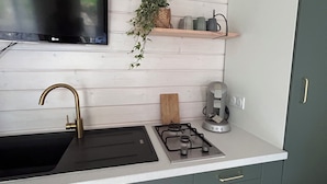 A kitchen with a black sink, a gas stove, a coffee maker, a television above the sink, and a wooden shelf with decorative items.