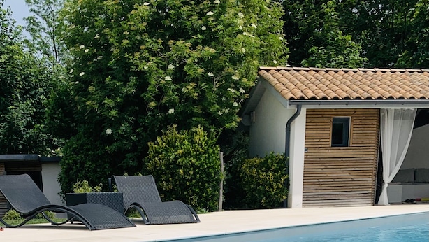 A swimming pool with lounge chairs, a wooden cabin, and lush greenery.
