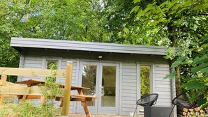 A wooden deck with a small building, a chair, and a wooden bench.