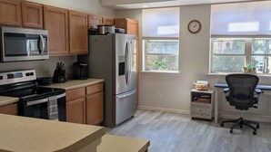 A modern kitchen with wooden cabinets, stainless steel appliances, a large window, and a small office area.