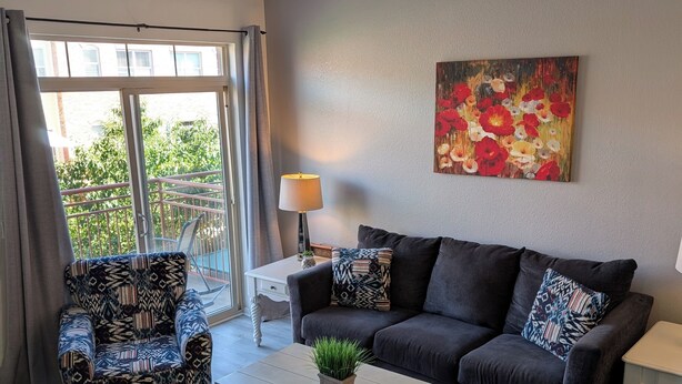 A modern living room with a grey sofa, patterned armchairs, a coffee table with a plant, and a painting on the wall.