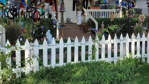 A house with a porch decorated with various items, a sign reading "Carly's Boutique," and a white picket fence.