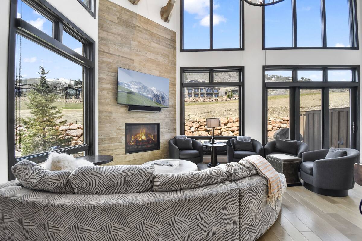 Una sala de estar moderna con chimenea, ventanas amplias y vistas a un paisaje montañoso.