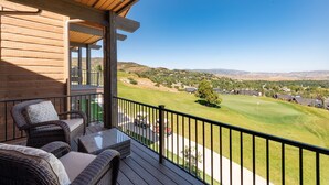 Una terraza de madera con mobiliario de mimbre, con vista a un campo de golf y una zona residencial.