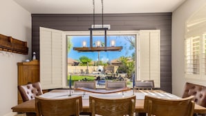 A dining area with a table and chairs, a view of a backyard with a pool and patio furniture, and a sign reading "VANDERHILL". - Ultimate AZ Getaway! Enjoy this Stunning 5BD with refreshing Pool & Spa! (Goodyear)