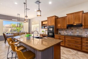 Enjoy cooking in this kitchen with a central island, sink, and bar stools, surrounded by cabinets and a mosaic tile backsplash.
