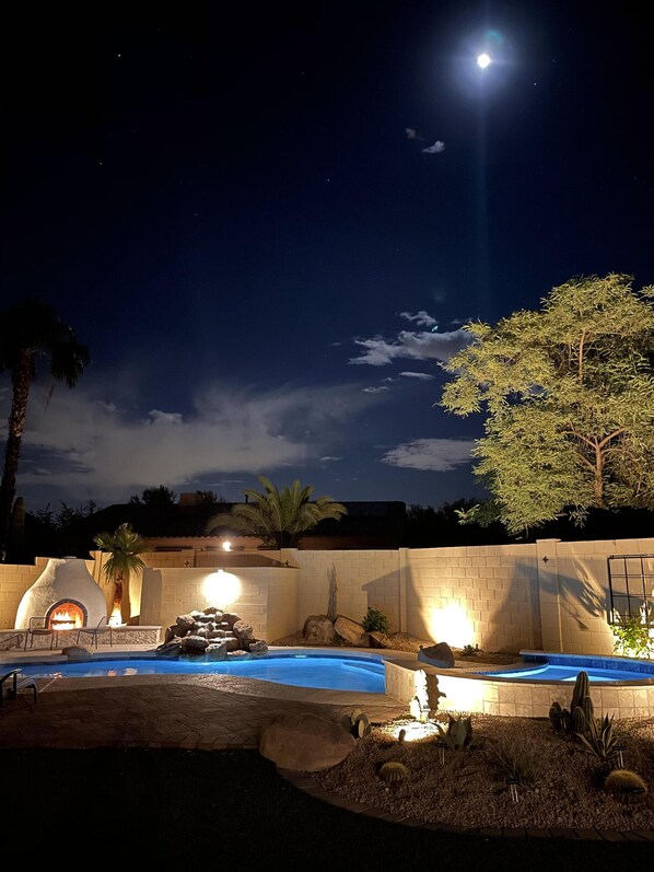 Relax by the outdoor fireplace surrounded by desert plants and a serene pool area.