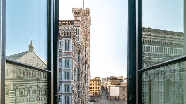 Vue depuis l’intérieur d’un bâtiment, à travers de grandes fenêtres, sur une rue bordée de bâtiments historiques.