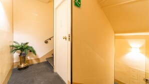 Un couloir d’hôtel avec un escalier, une plante en pot et une signalisation indiquant les issues de secours.