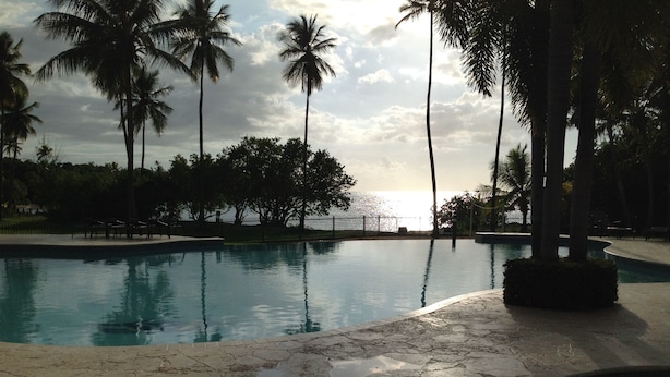 A swimming pool with a view of the sunset, surrounded by palm trees and a fence. - Beachfront family friendly garden condo, full A/C, WiFi, sleeps 6, Smart TV's (Cabo Rojo)