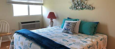 Une chambre à coucher comprenant un lit, une chaise, un élément de décoration murale et une fenêtre avec des stores.