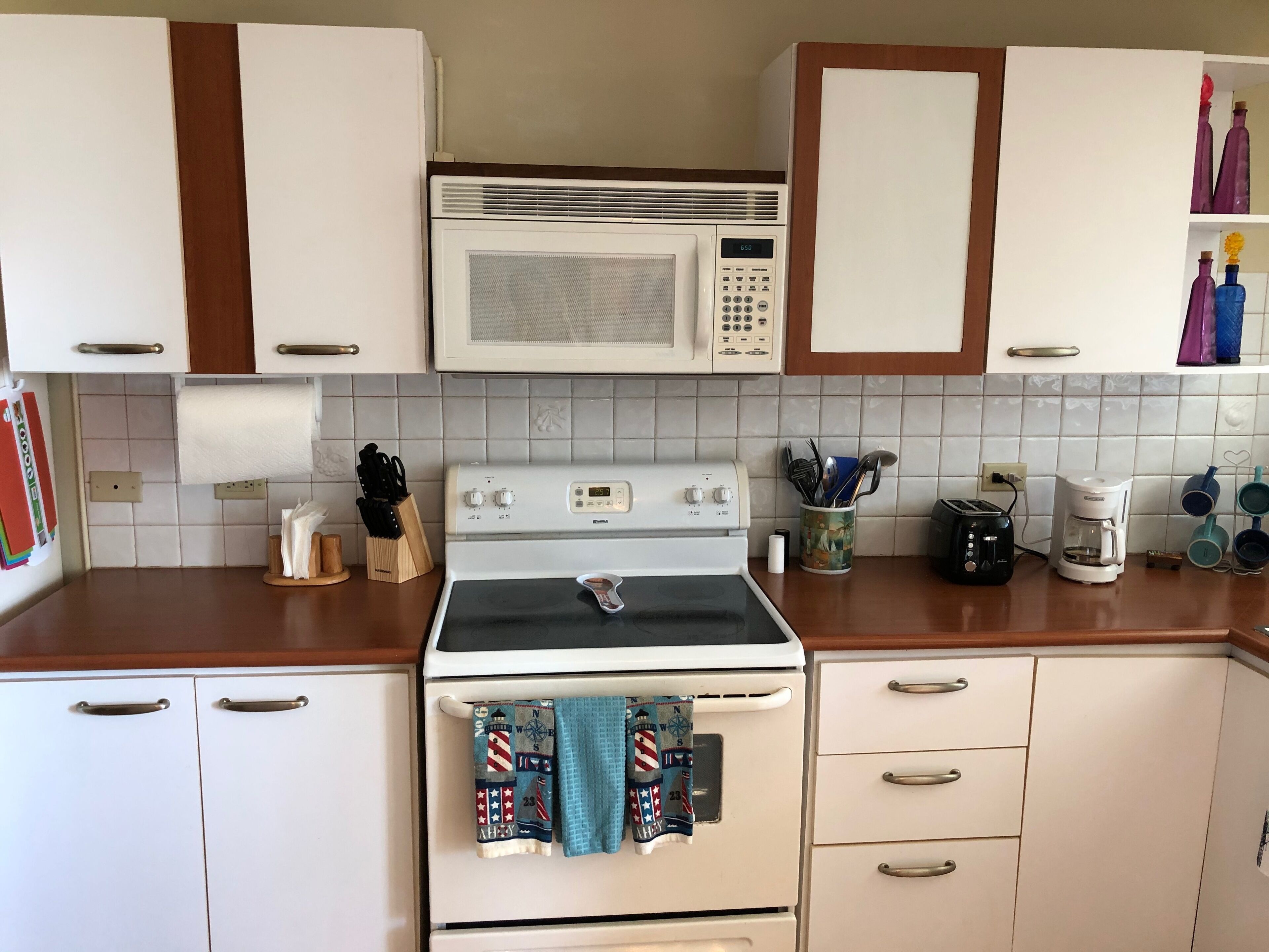 Une cuisine avec des meubles blancs, un four à micro-ondes, une cuisinière et une machine à café.
