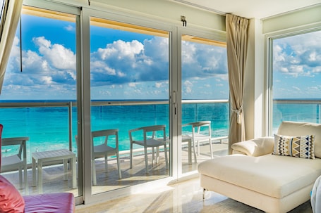 A balcony with a view of the ocean, a white sofa, and several chairs.