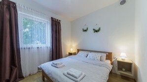 Un lit bien fait, recouvert d’une couvre-lit à motifs géométriques et agrémenté de deux oreillers, une table de chevet avec une lampe, et une fenêtre avec des rideaux.