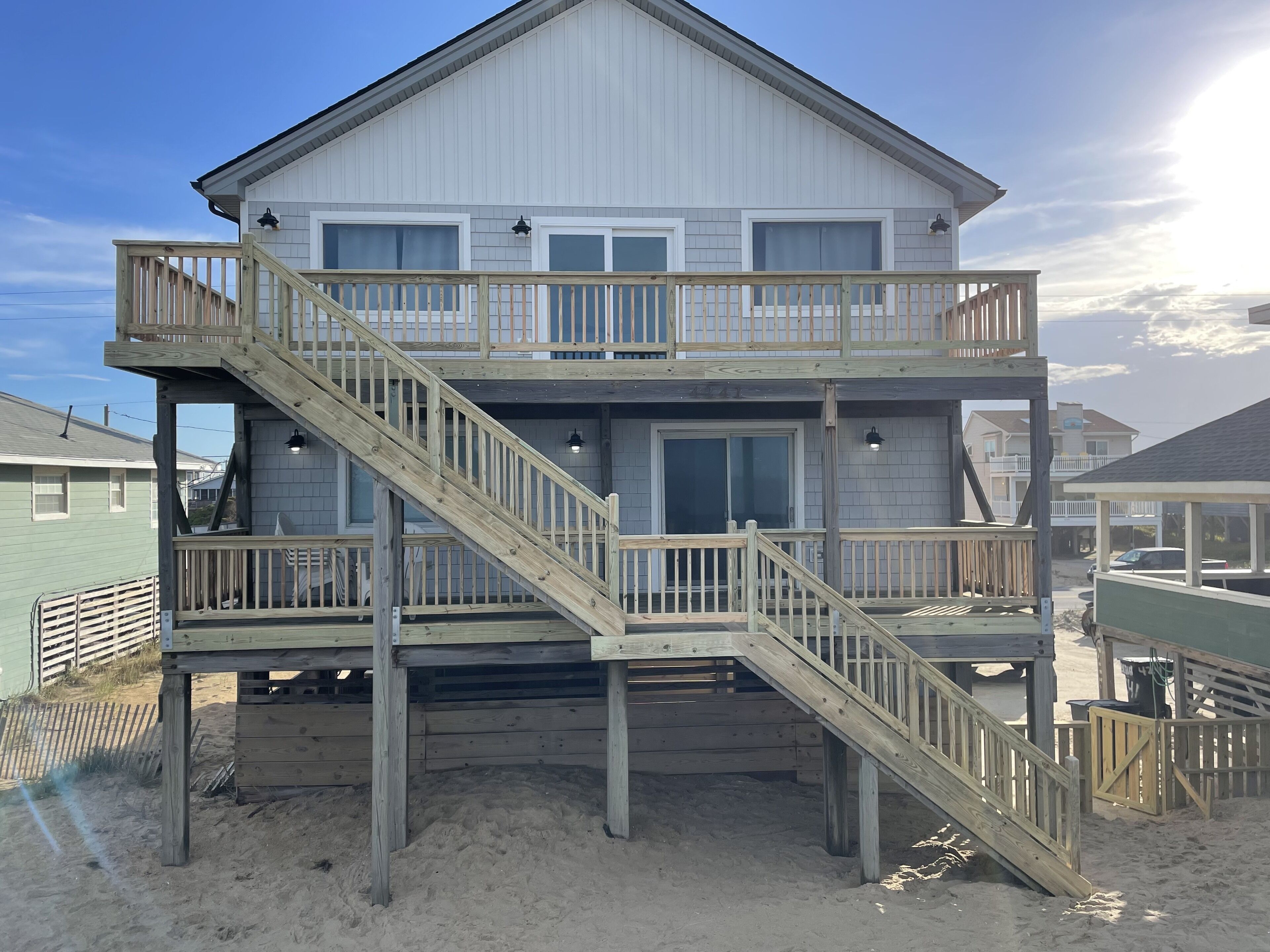 Une maison à deux étages située en bord de mer, dotée d’une terrasse en bois et d’un escalier menant à l’étage supérieur.