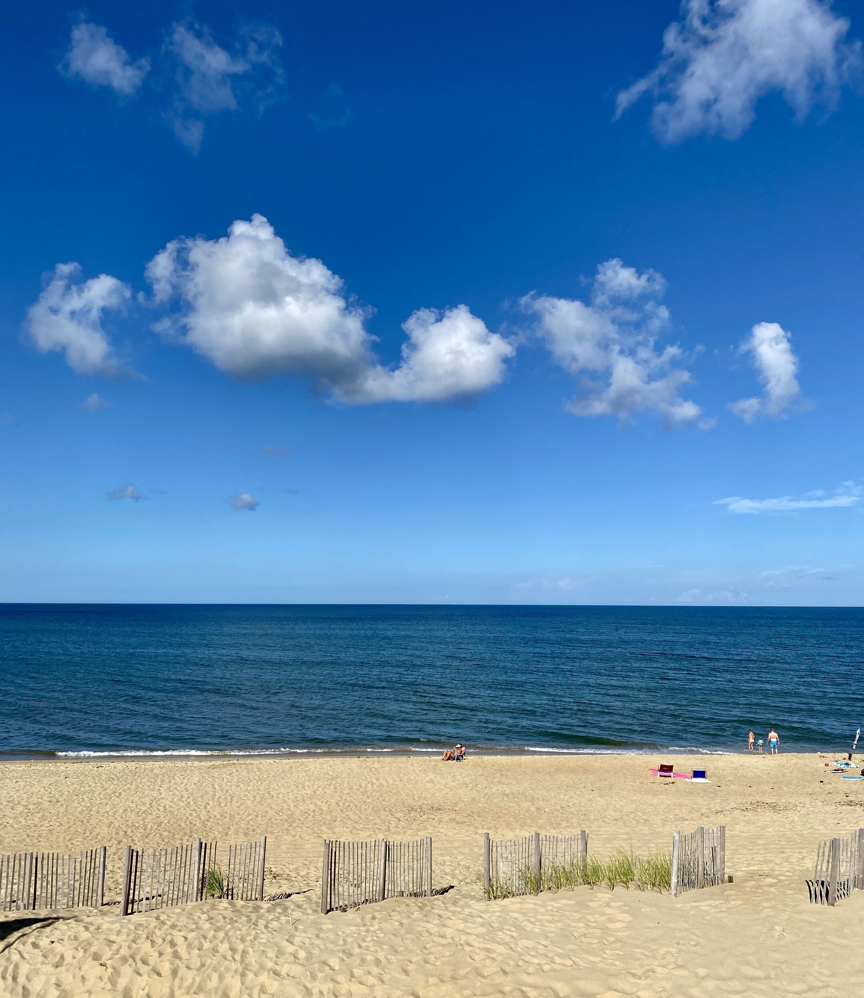 Ein Strand mit Holzlattenzaun, blauem Himmel und dem Meer.