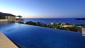 Una piscina infinita moderna con una vista despejada del océano y la costa lejana.