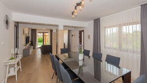 A spacious dining area with a long table and chairs, a modern chandelier, and a view of a garden through large windows. - Awesome home in Sibenik (Sibenik)