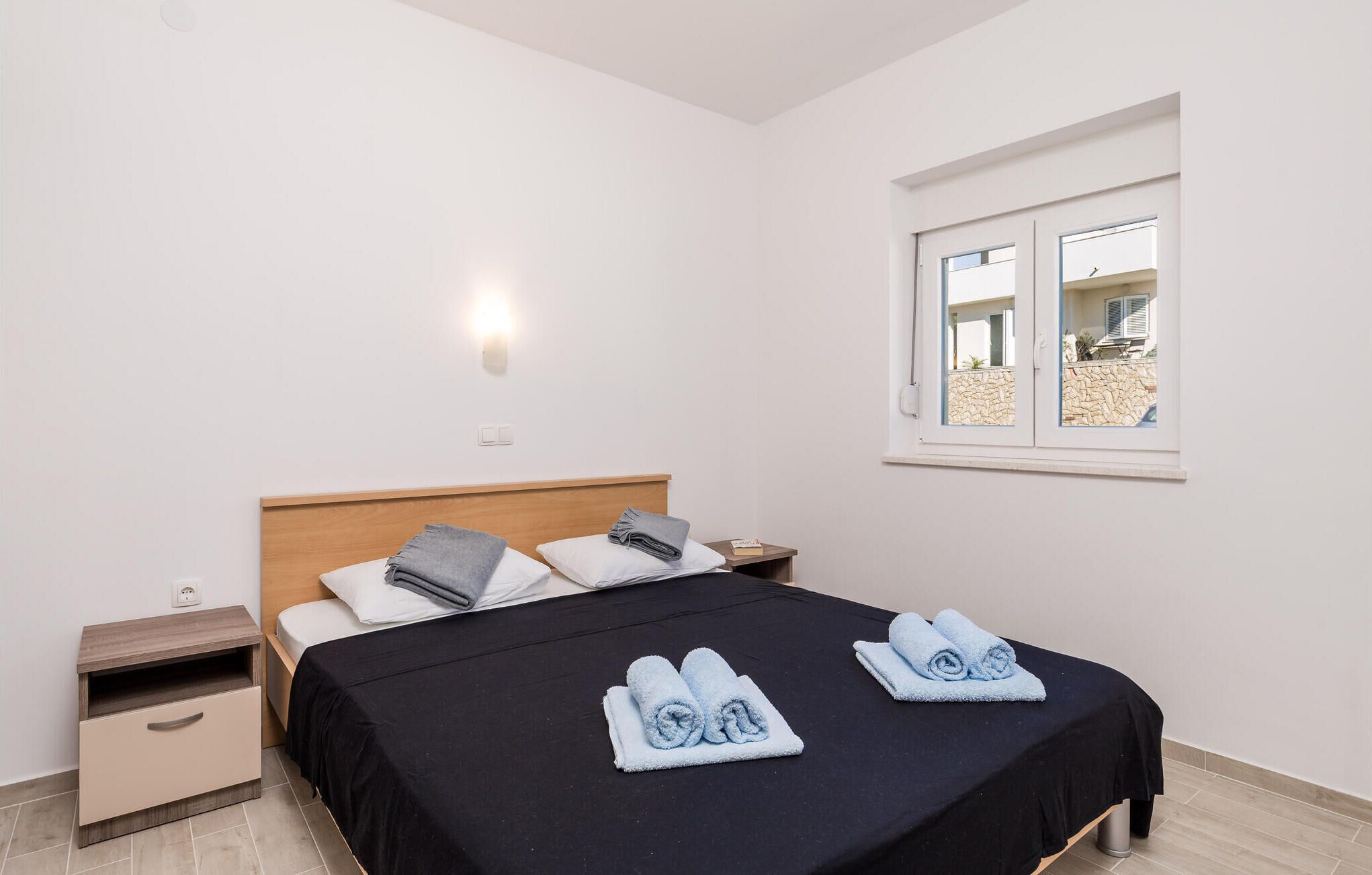 Una habitación de hotel con una cama, una mesita de noche, una ventana y una lámpara fijada a la pared.