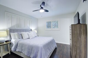 A bedroom with a bed, a ceiling fan, a nightstand, a dresser, and a window with blinds. - Heart of NPB: Your Perfect Home Away from Home! (North Palm Beach)