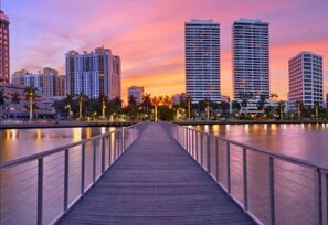 A waterfront promenade with a wooden walkway, tall buildings, and palm trees. - Heart of NPB: Your Perfect Home Away from Home! (North Palm Beach)