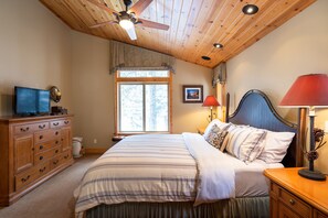 Een slaapkamer met een bed, een houten dressoir, een plafondventilator, een raam en nachtlampjes.