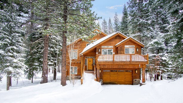 Eine Holzhütte mit Veranda und Garage, umgeben von schneebedeckten Bäumen.
