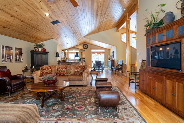 A spacious living room with a high wooden ceiling, a large TV, and a cozy seating area with a patterned rug.