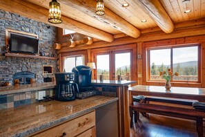 A rustic kitchen with stone walls, a coffee maker, and a dining area with a view. - Log Cabin with Breathtaking Views, Dogs OK (Fairplay)