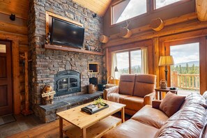 A cozy cabin interior with a stone fireplace, leather sofa, wooden coffee table, and a television mounted on the wall. - Log Cabin with Breathtaking Views, Dogs OK (Fairplay)