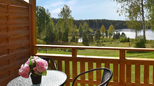 Puinen terassi, jossa on lasipöytä ja -tuolit, ja jolta avautuu näkymä järvelle ja metsään.