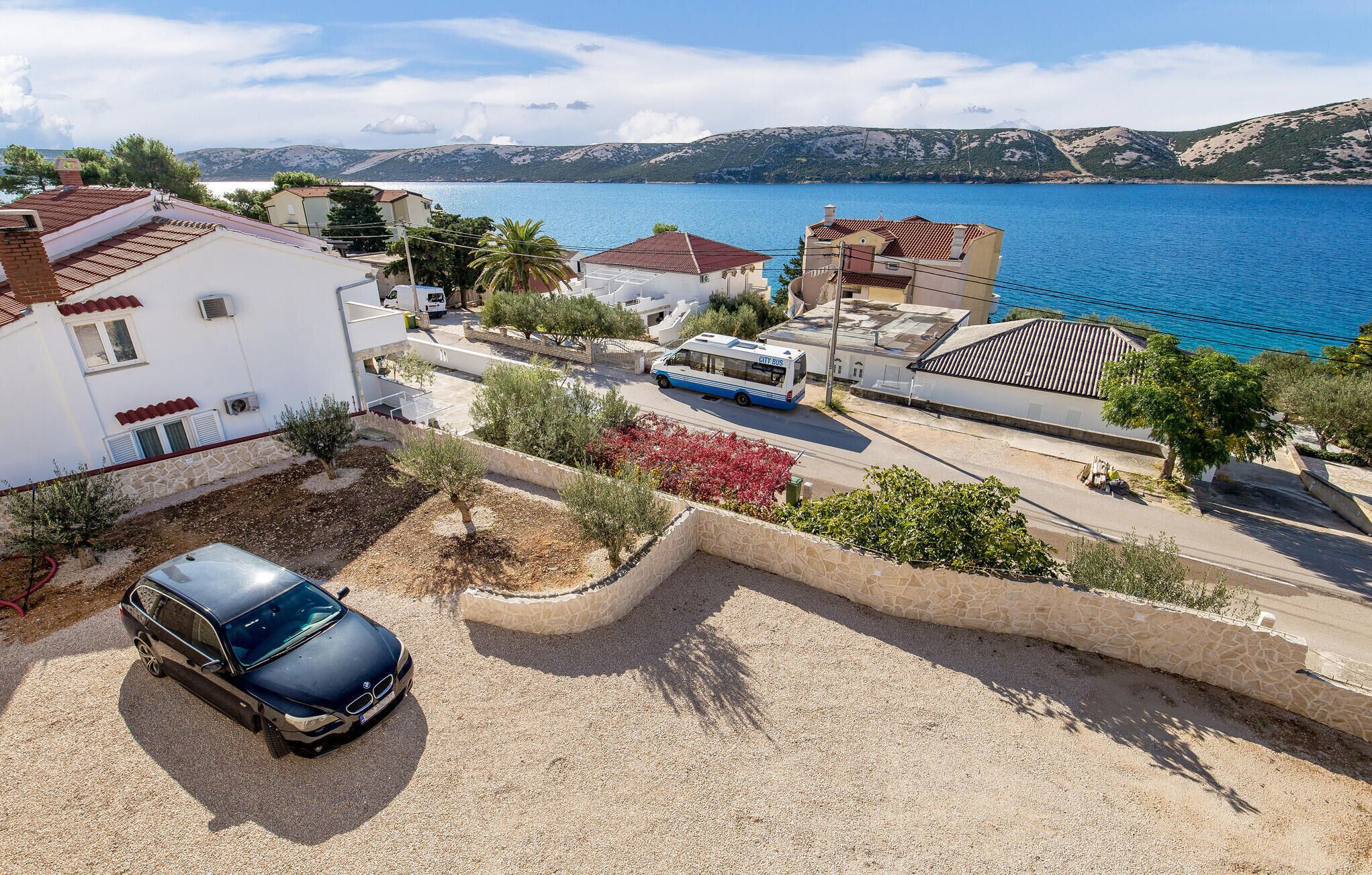 A coastal residential area with a parked car, a bus, and houses with Mediterranean architecture.