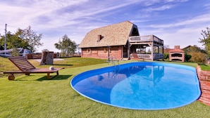 En swimmingpool med ett trädäck, ett hus byggt av tegel och en täckt uteplats.