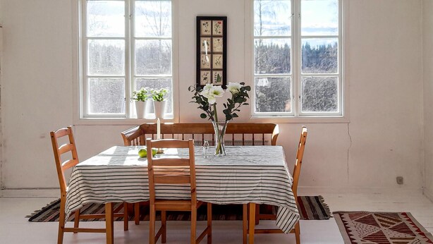 Un comedor con una mesa dispuesta para cuatro personas, rodeada de sillas de madera, un florero con flores e impresión botánica enmarcada en la pared.