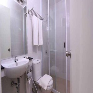 A bathroom with a sink, mirror, towel rack, toilet, and glass shower enclosure. - Evan Hotel Jambi (Jambi)