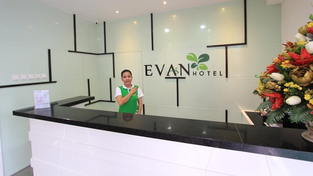 A hotel reception desk with a receptionist, a sign reading "EVAN HOTEL", and a decorative floral arrangement.
