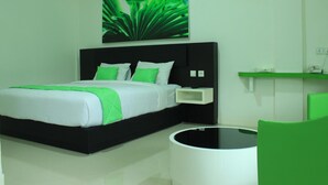 A modern hotel room with a black bed frame, white bedding, and green accents.