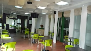 A modern dining area with green chairs and tables, a projector on the ceiling, and a view of the dining area in the background.