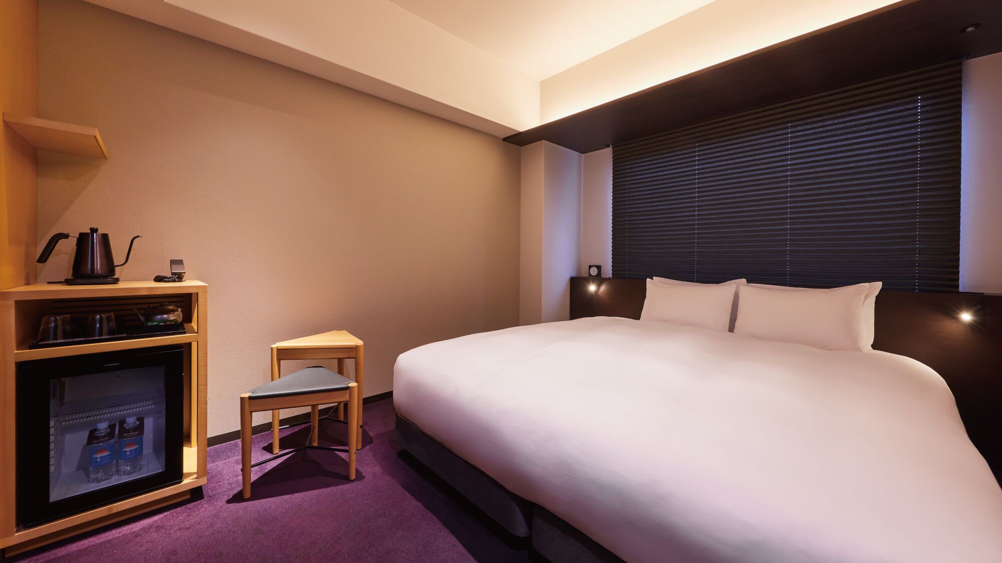 Una camera d'albergo con un letto, un tavolino, un frigorifero e una macchina del caffè.