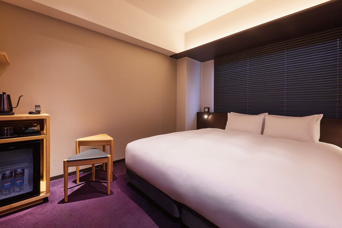 A hotel room with a bed, a small table, a refrigerator, and a coffee maker.