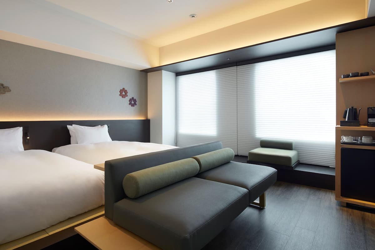 Une chambre d’hôtel moderne équipée de deux lits, d’un canapé, d’une petite table et d’une kitchenette.