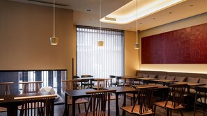 A modern dining area with wooden tables and chairs, large windows with blinds, and a red accent wall. - Agora Kyoto Shijo (Kyoto)