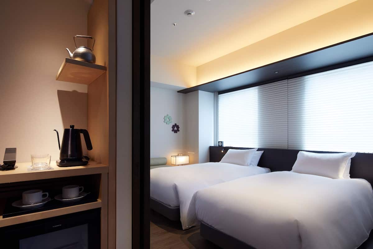 Une chambre d’hôtel avec deux lits, une machine à café, une petite table avec des tasses et un téléviseur.