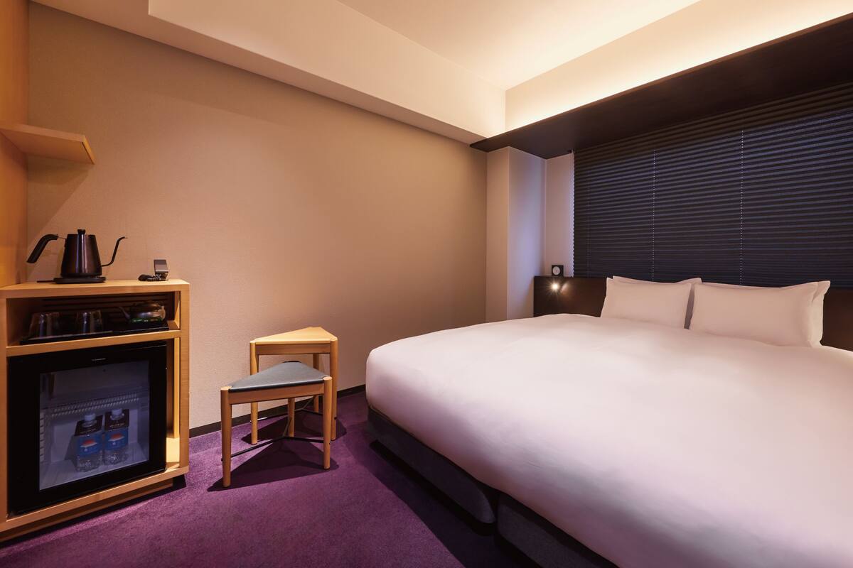 Une chambre d’hôtel comprenant un lit, une petite table avec une bouilloire, une chaise et un mini-bar.