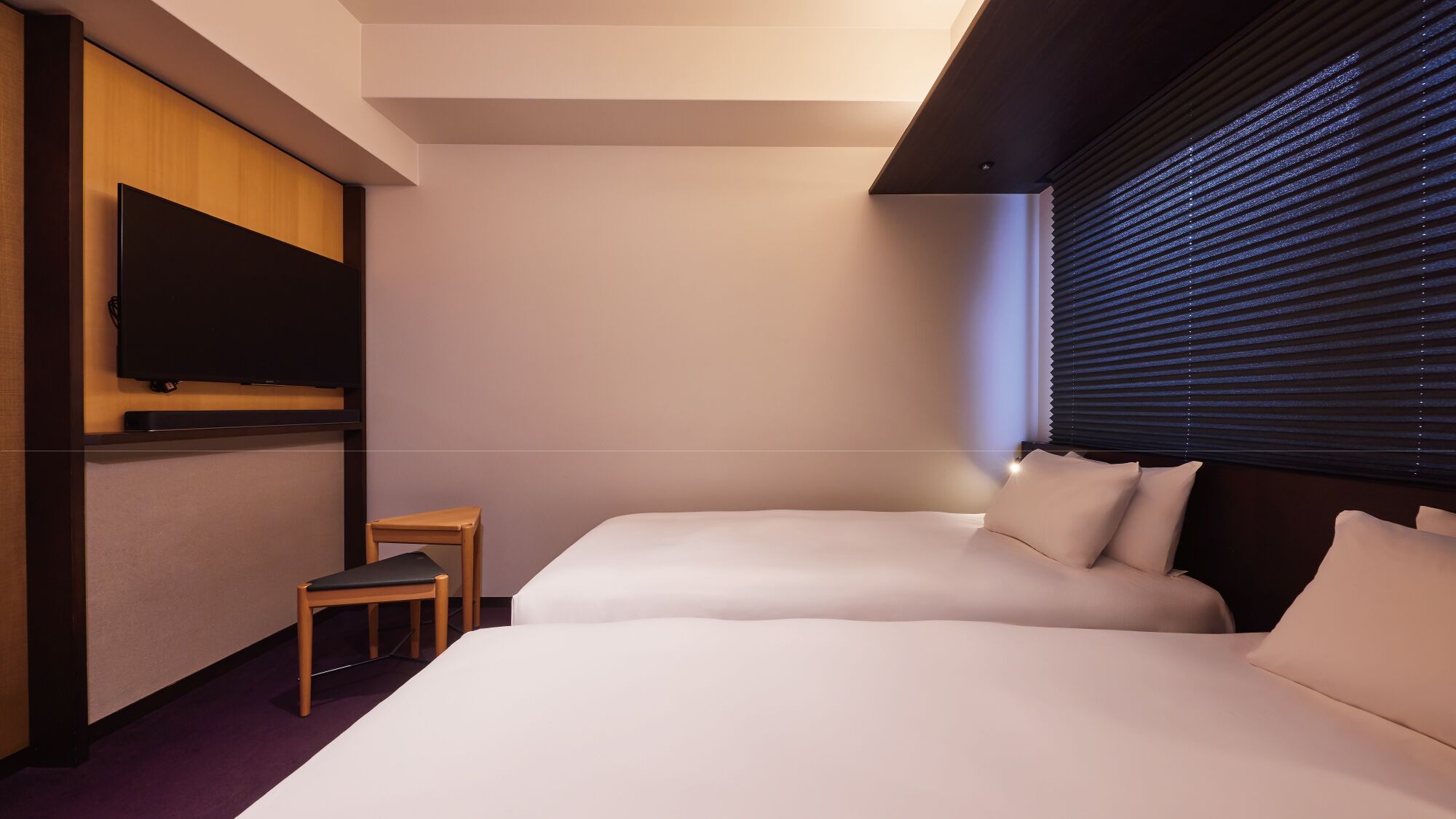 Una camera d'albergo con un letto, una televisione, un tavolino e una finestra con persiane.