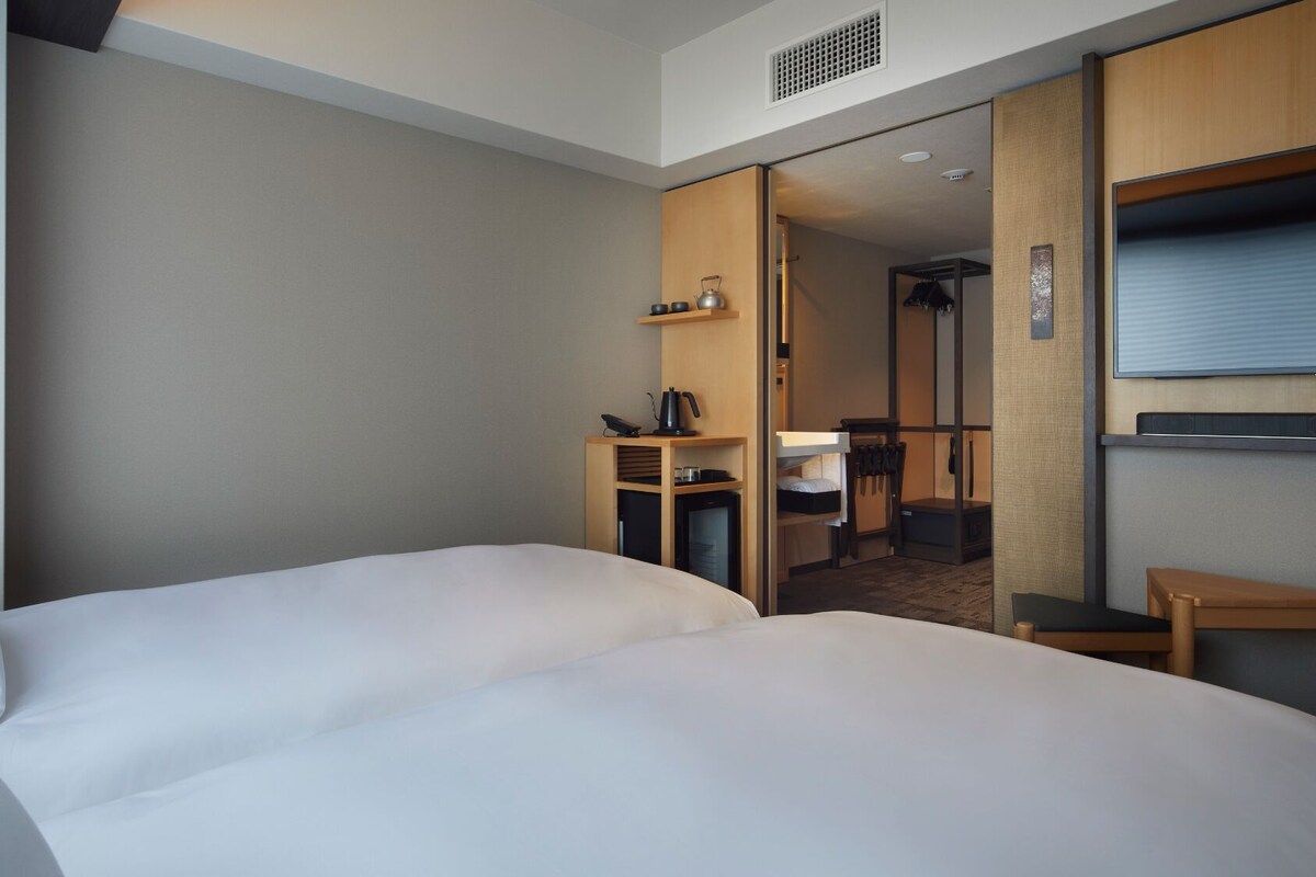 A hotel room with a large bed, a desk with a kettle, and a TV.