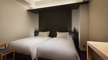 A hotel room with two beds, a desk, and a window with blinds.