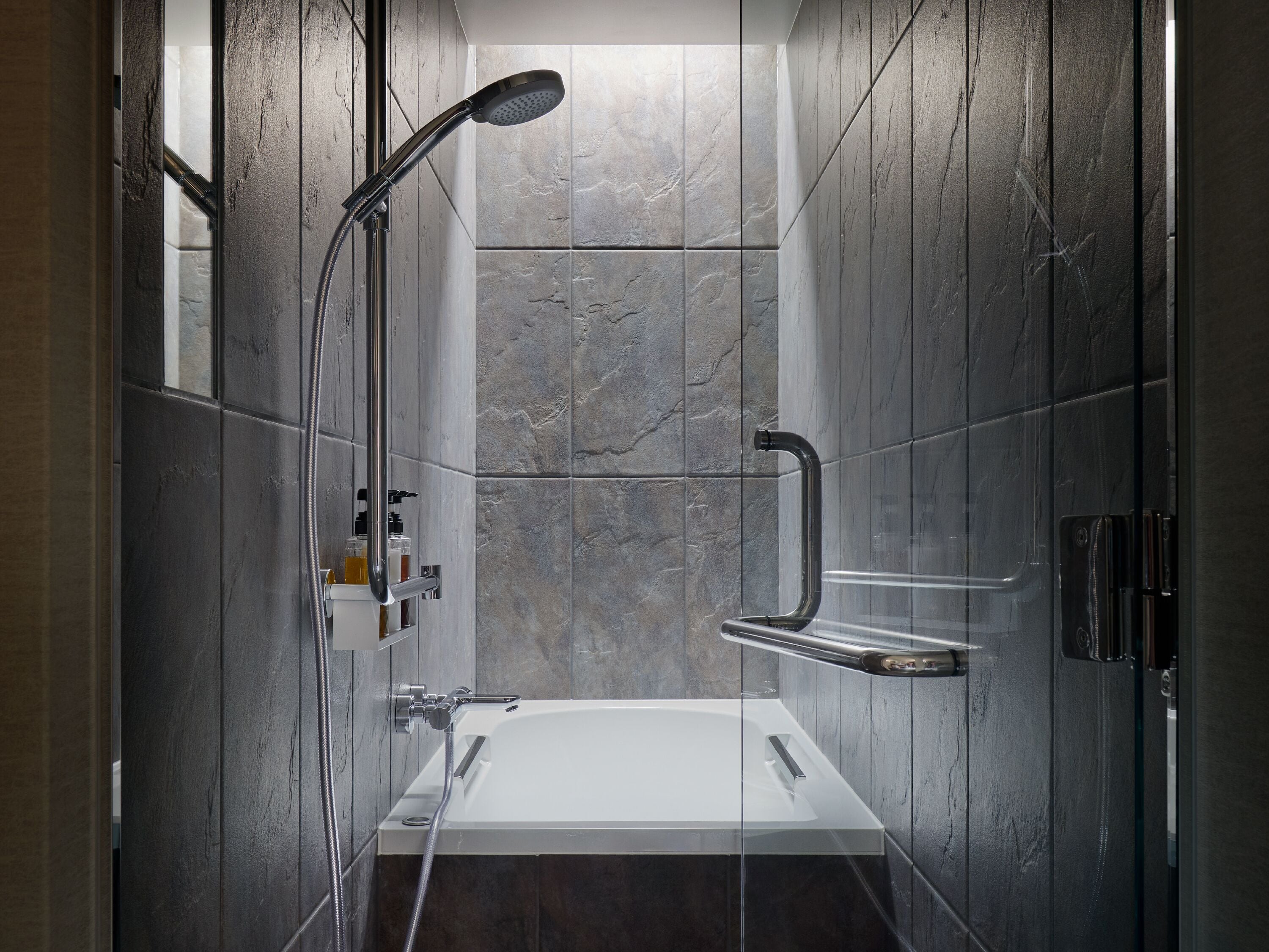 A modern bathroom with a glass-enclosed shower, a white bathtub, and a built-in shelf with toiletries.